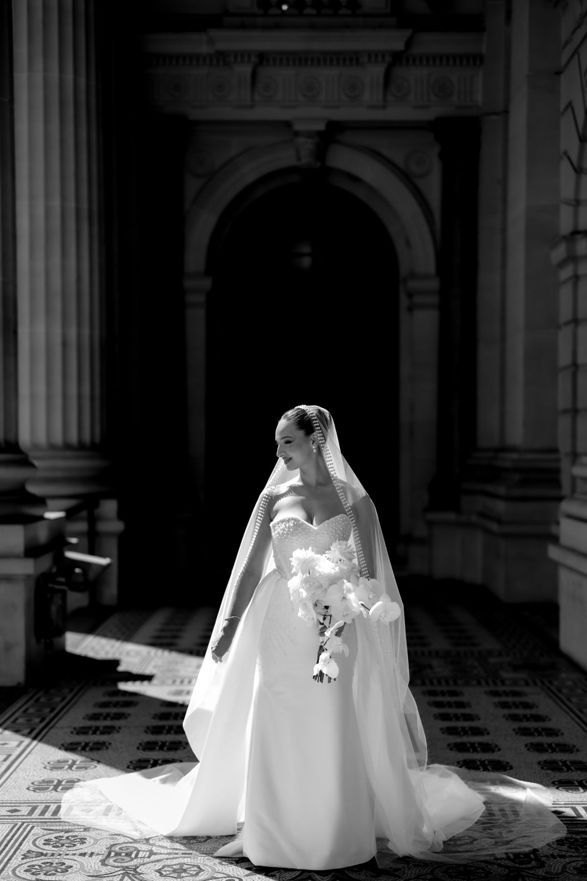 Bride standing in a shaft of light in a dark stone portico