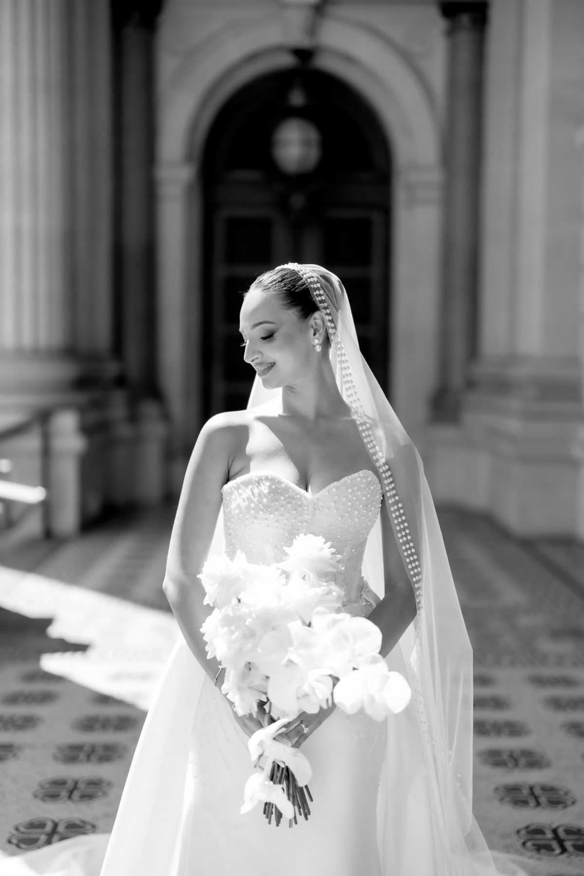 Bride in a pearl-trimmed veil looking down at her bouquet