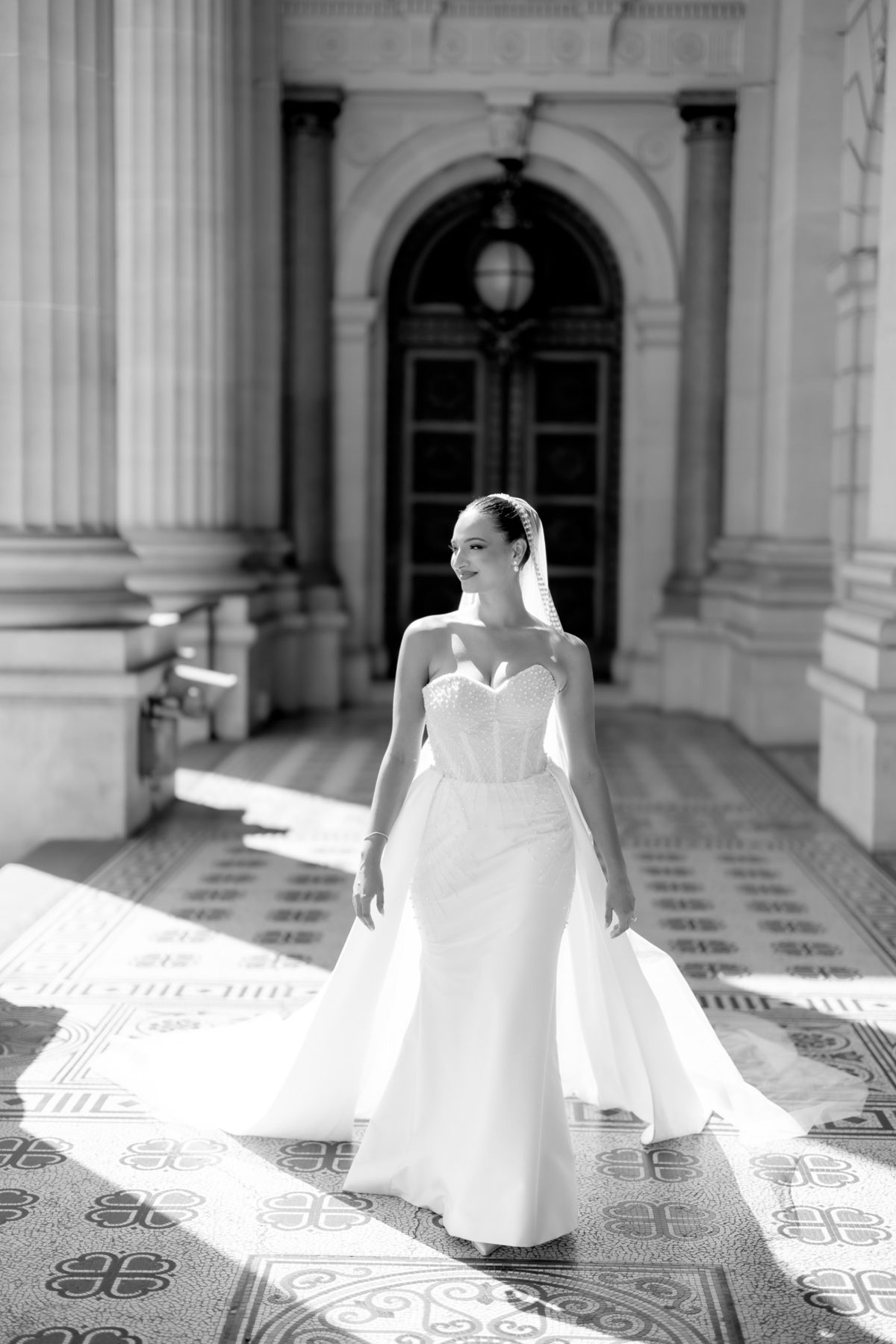 Melbourne wedding photographer captures a bride smiling as she walks through a sunlit stone portico