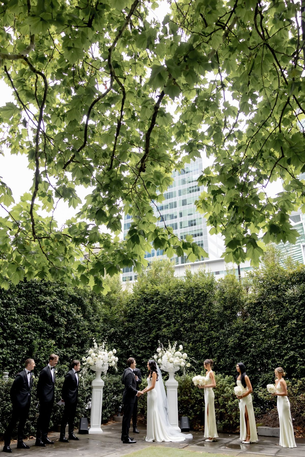 Courtyard ceremony under a leafy canopy with the bridal party lined up either side