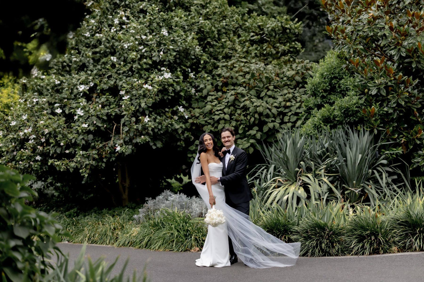Film still of the couple laughing in a lush garden as her veil streams out in the breeze