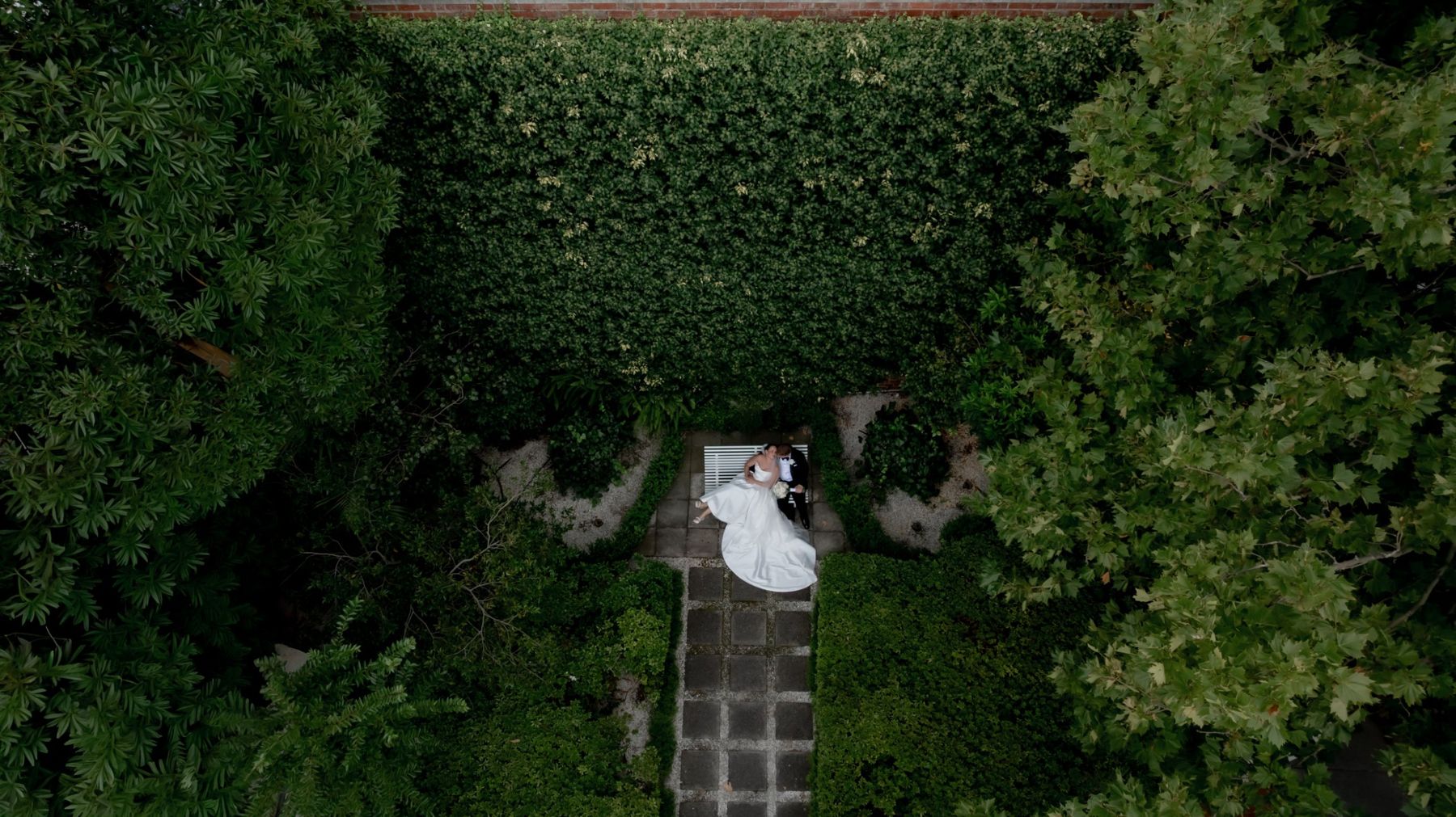 Drone wedding photography: overhead shot of the couple and her gown framed by lush greenery
